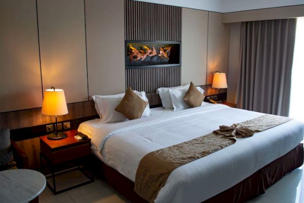 A cozy hotel room features a large bed, pillows, two lamps, a wall feature, side tables, and a window with curtains.