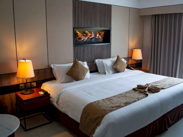 A cozy hotel room features a large bed, pillows, two lamps, a wall feature, side tables, and a window with curtains.