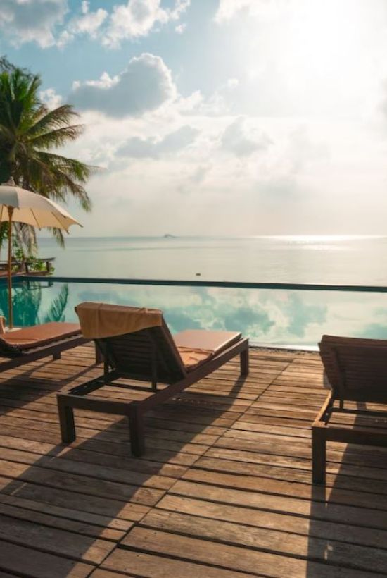 Beachside deck with lounge chairs, umbrellas, and a view of the ocean under a sunny sky.