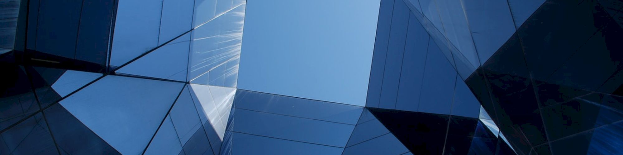 The image shows an upward view of mirrored skyscrapers reflecting the sky, creating a geometric pattern with a central blue sky opening.