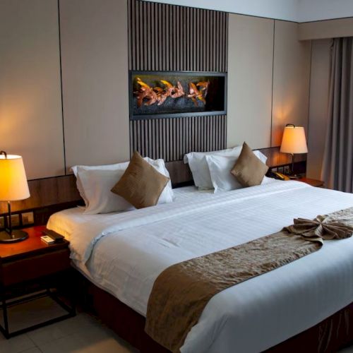 A cozy hotel room with a large bed, two bedside lamps, decorative pillows, curtains, and a modern wall art piece above the bed.