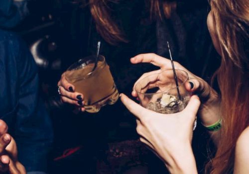 People enjoying drinks and conversation at a social gathering or party, with visible laughter and gestures.