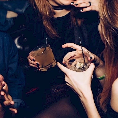 People enjoying drinks and conversation at a social gathering or party, with visible laughter and gestures.