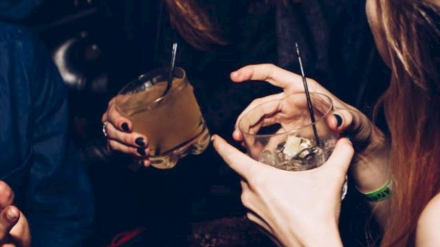 People enjoying drinks and conversation at a social gathering or party, with visible laughter and gestures.