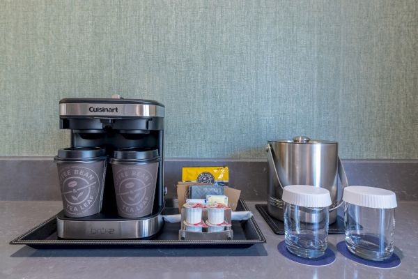 A coffee maker with cups, creamers, a tea bag, ice bucket, and glasses on a counter.