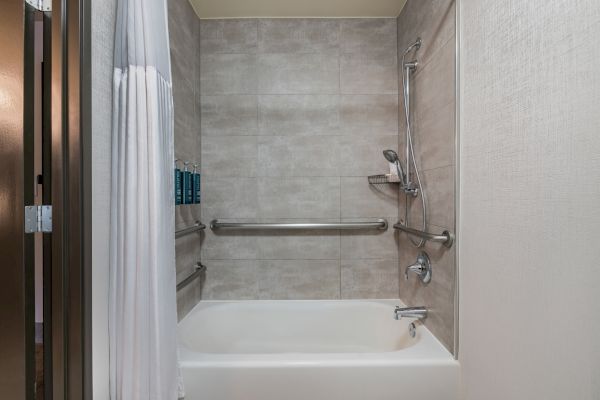A bathroom with a bathtub, showerhead, shower curtain, and wall-mounted shampoo dispensers, featuring handrails for accessibility.