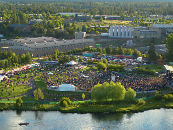 An aerial view of an outdoor concert with large crowds, tents, and surrounding greenery near a river.