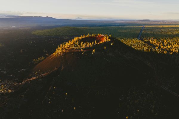 The image shows an aerial view of a volcanic crater surrounded by a forested landscape with trees and natural vegetation.