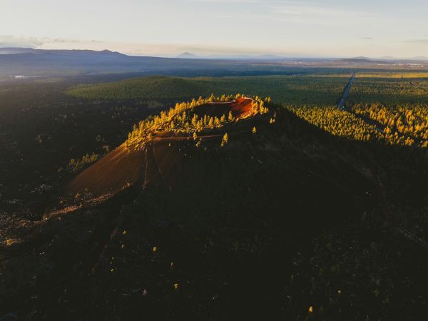 The image shows an aerial view of a volcanic crater surrounded by a forested landscape with trees and natural vegetation.