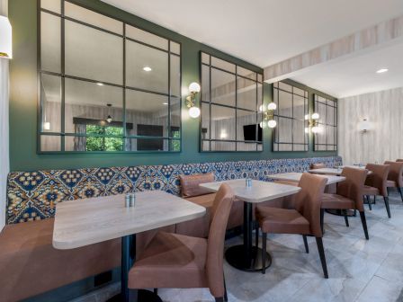 The image shows a modern restaurant interior with tables, brown chairs, decorative tiles, large mirrors, and wall lights.
