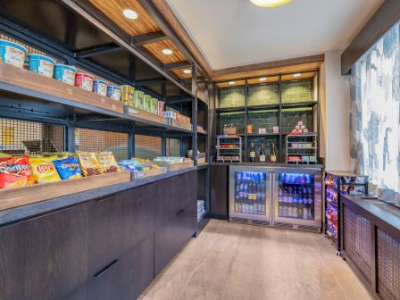 The image shows a small store with shelves of snacks, drinks, and refrigerated items, brightly lit, with a modern and organized setup.
