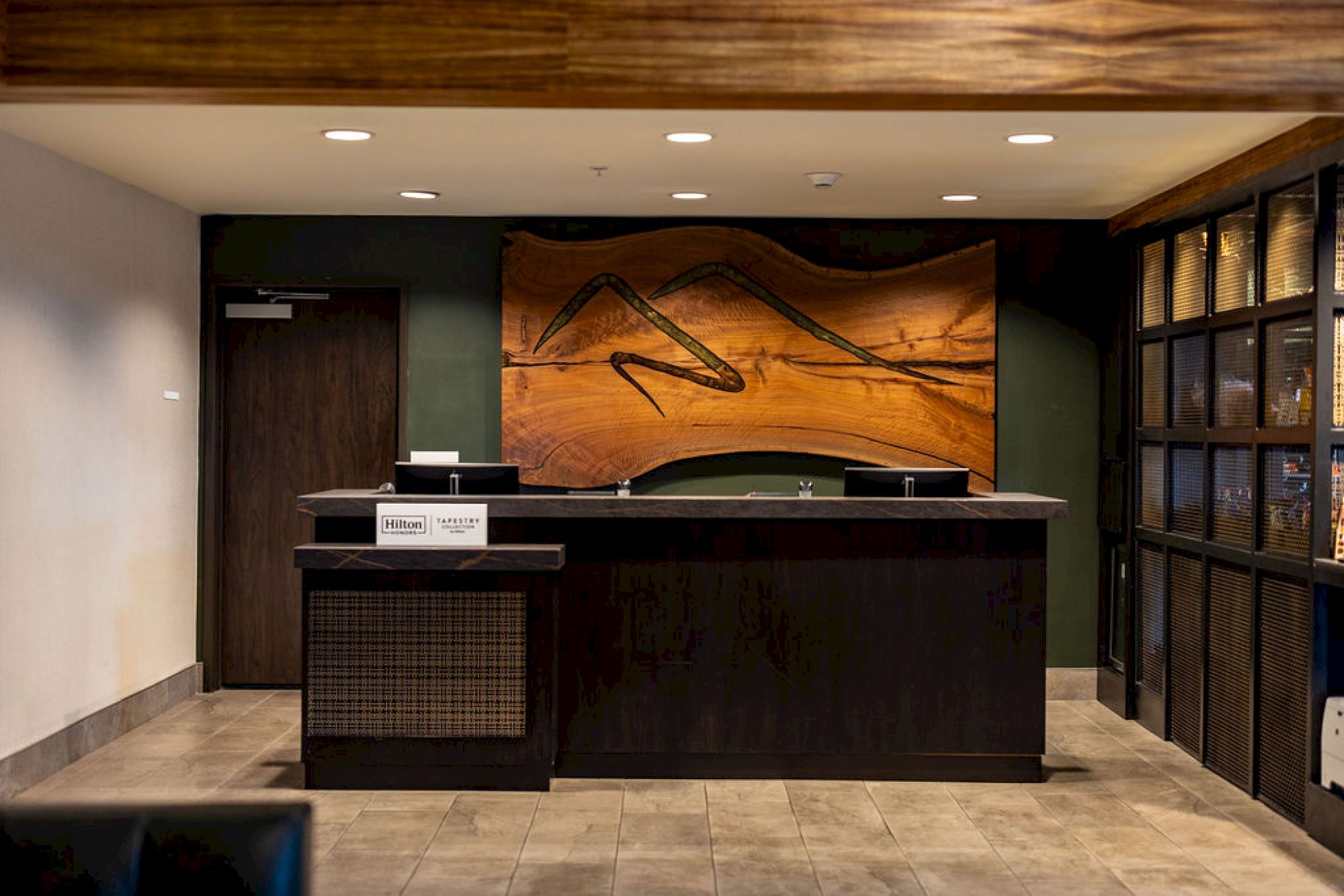 A hotel reception desk with a wooden wall art behind it and a card reader on the counter, in a modern lobby.