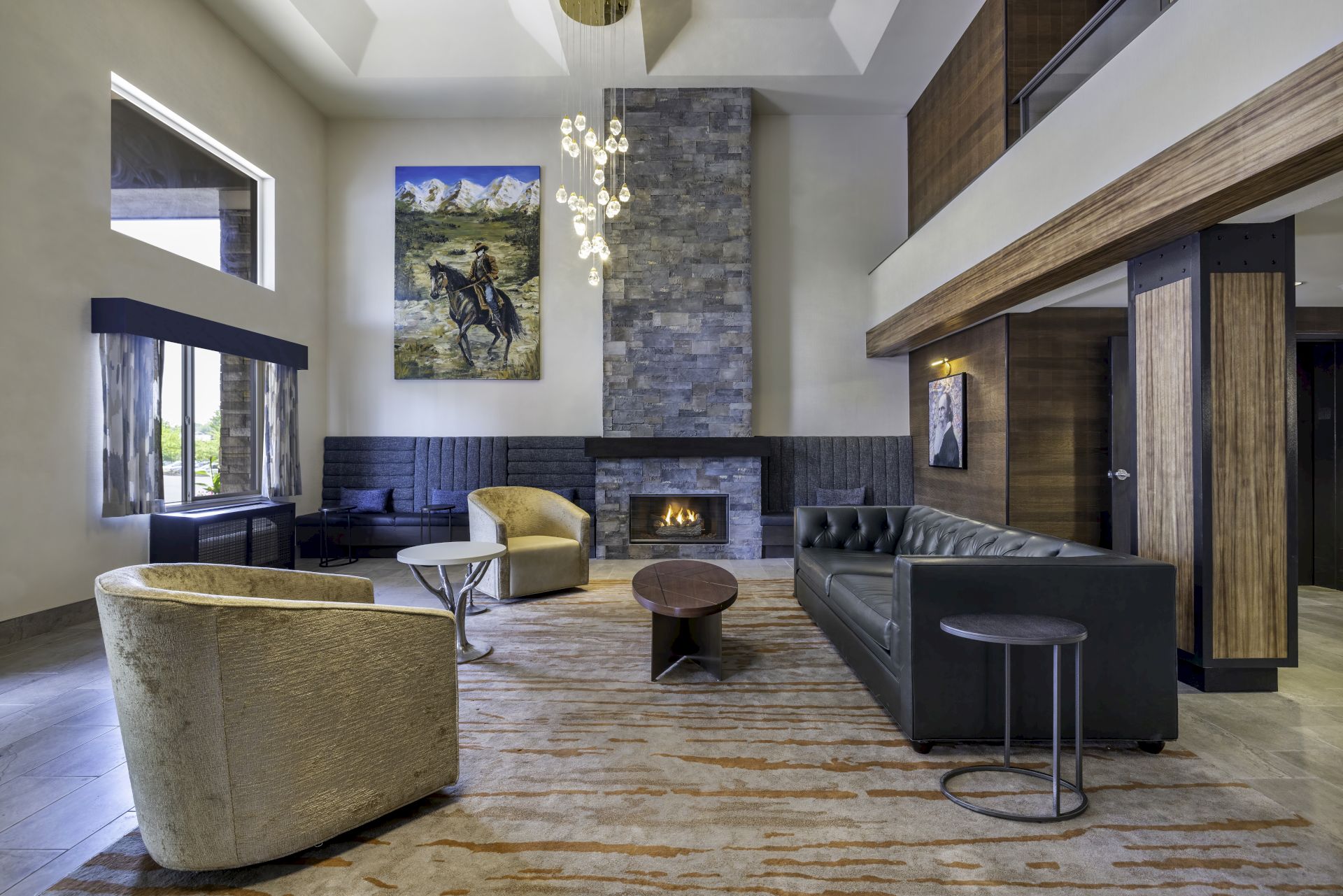 A modern living room with a high ceiling, stone fireplace, abstract art, and plush seating including a black sofa and round chairs.