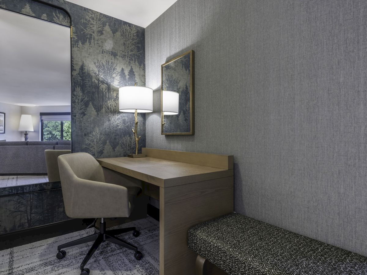 A stylish room with a desk, chair, mirror, and wall lamp, featuring patterned wallpaper and a bench in a modern design.