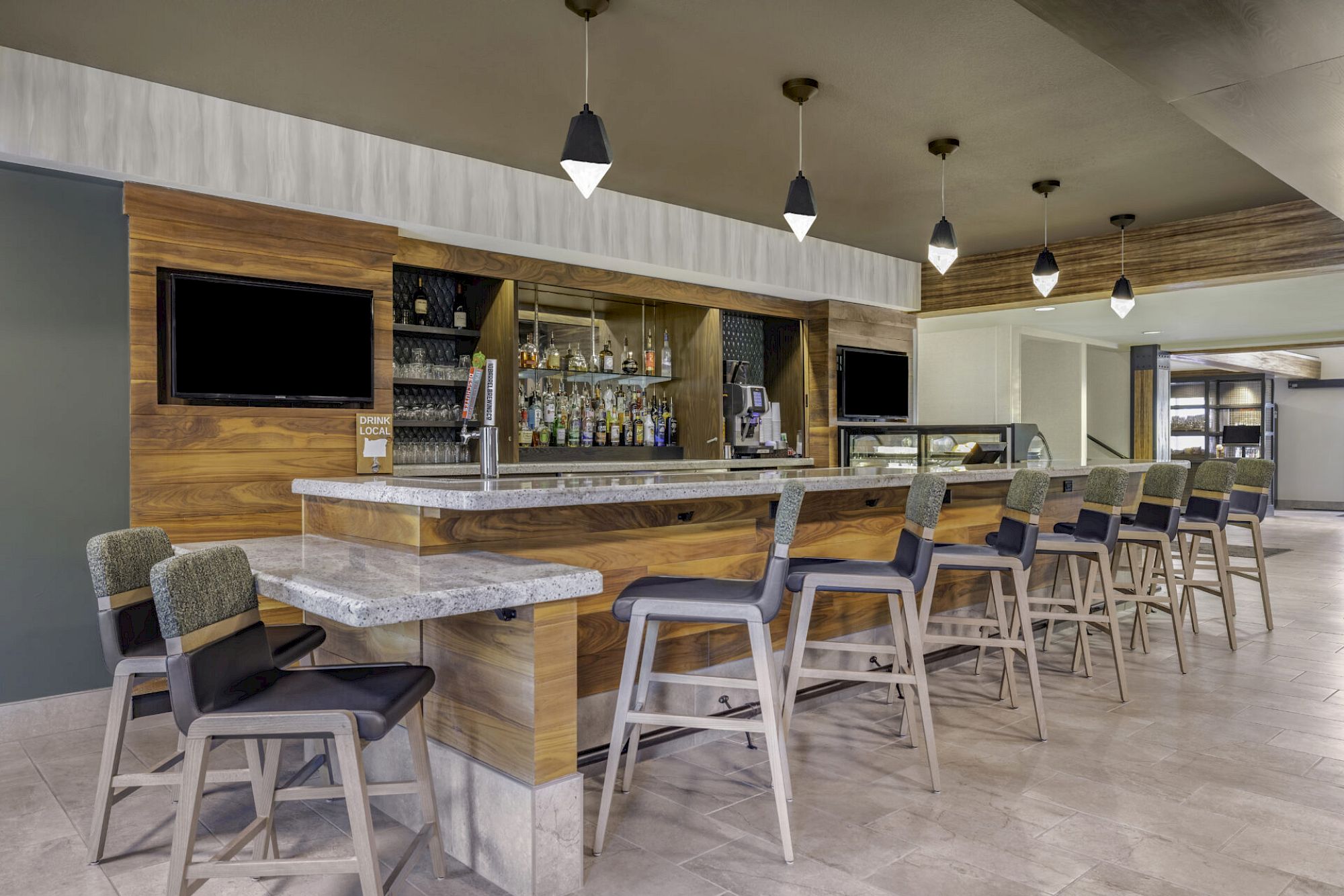 A modern bar setup with high chairs, hanging lights, and a stocked counter in a contemporary setting.