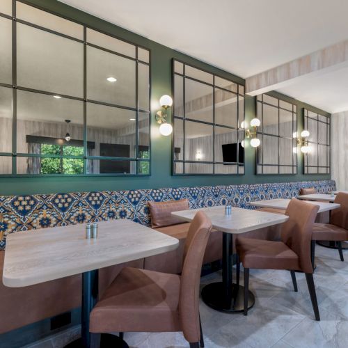 The image shows a modern dining area with patterned tiles, mirrors, and brown chairs around tables in a stylish, well-lit setting.