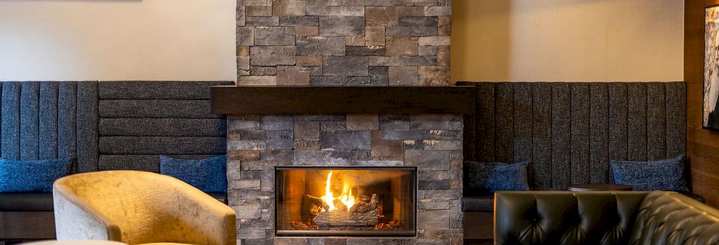 A cozy lounge with a stone fireplace, wooden accents, and comfortable seating around a warm fire, inviting relaxation.
