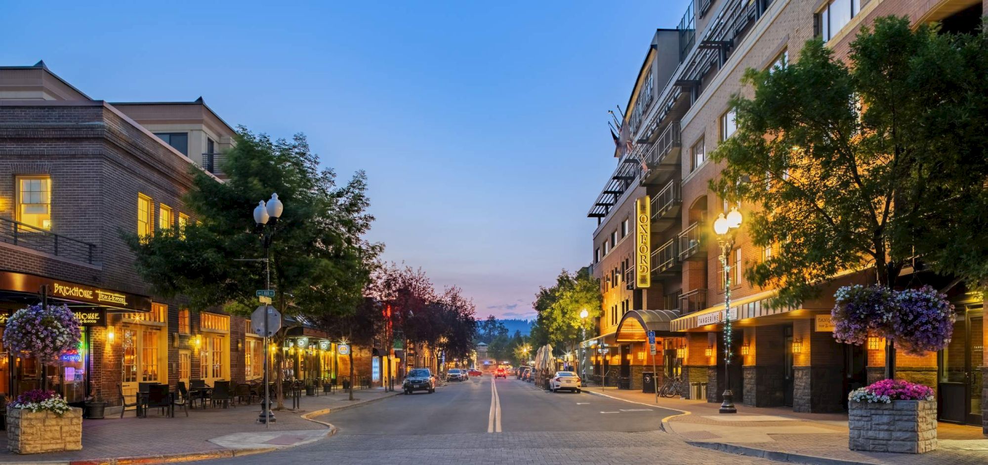 A peaceful downtown street at dusk with lined shops, warm lights, and trees framing the avenue.Top it at 140 characters, always ending the sentence.
