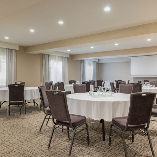 A conference room with round tables, beige walls, and a projector screen, set for a meeting or event.