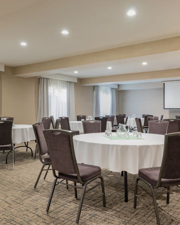A conference room with round tables, beige walls, and a projector screen, set for a meeting or event.