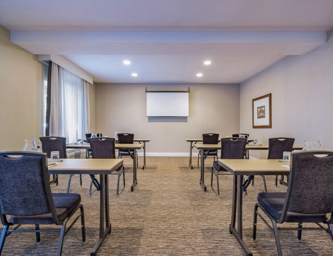 The image shows a small conference room with tables and chairs arranged in a classroom style setup, ready for a meeting or presentation.