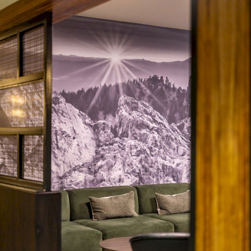 A cozy lobby with a green sofa, a round coffee table, and a black-and-white mountain mural on the wall, framed by wooden panels.