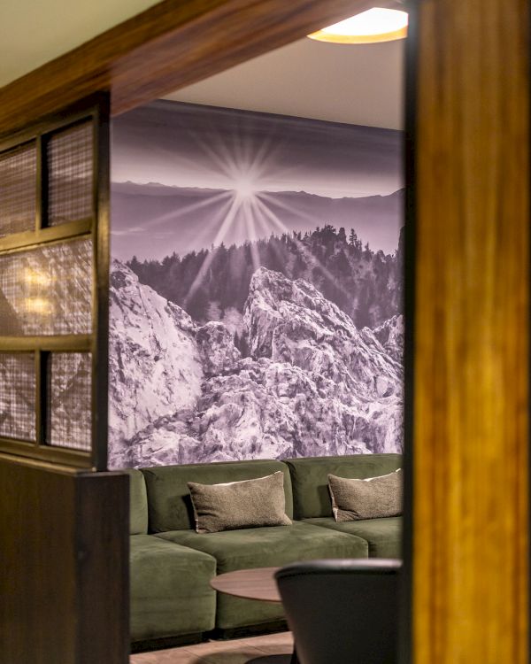 A cozy lobby with a green sofa, a round coffee table, and a black-and-white mountain mural on the wall, framed by wooden panels.