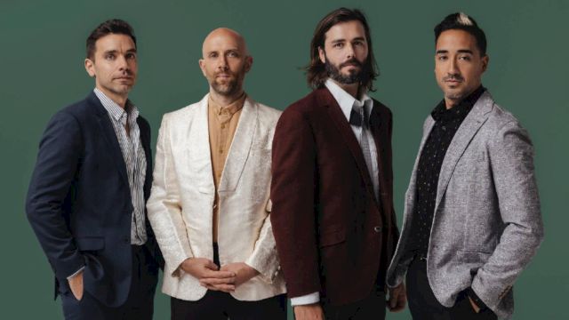 A four-member manly group posing in stylish suits against a green backdrop.