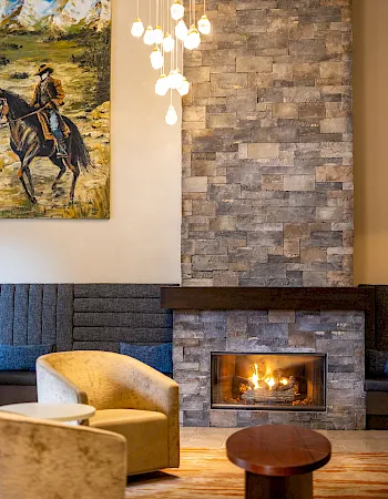 A cozy living room with a stone fireplace glowing, blue sofas, a wooden coffee table, and a mountain painting above the seating.