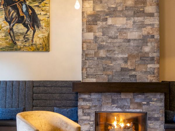 A cozy living room with a stone fireplace, hanging lights, blue seating, and a landscape painting on the wall.