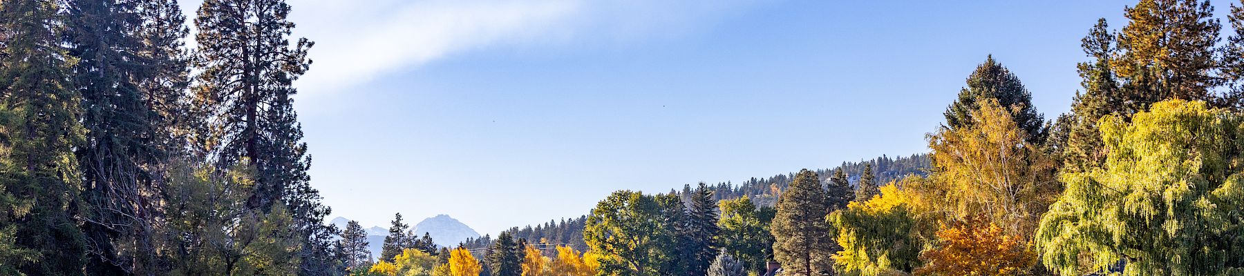 A calm lake with reflections, surrounded by autumn trees and distant hills under a blue sky with wispy clouds.