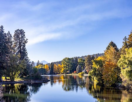 A calm lake with reflections, surrounded by autumn trees and distant hills under a blue sky with wispy clouds.