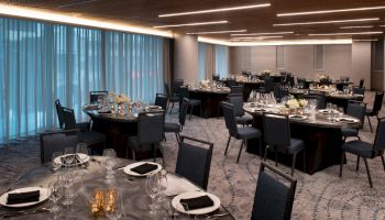 The image shows an elegant banquet room with round tables set for a formal event, featuring black chairs and dim lighting.