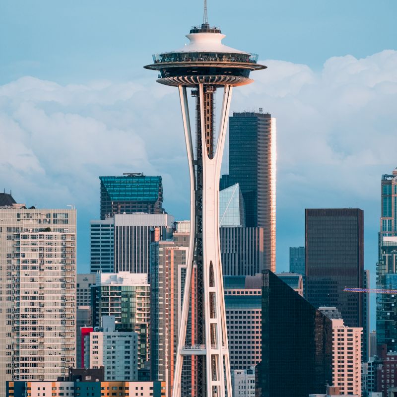 The image shows a city skyline featuring a famous tower with a saucer-shaped top, surrounded by various skyscrapers under a blue sky.