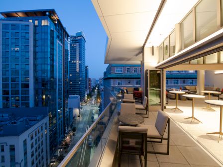 A modern rooftop terrace with seating, overlooking a city street lined with tall buildings during twilight.