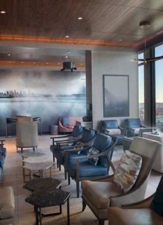 A modern lounge with multiple chairs, tables, and large windows overlooking a scenic view of water and a distant Ferris wheel.