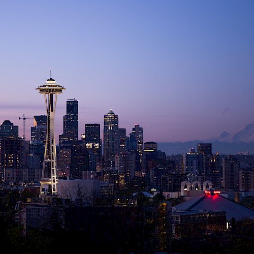 Seattle skyline at dusk with the Space Needle and Mount Rainier in the background, featuring city lights and a clear sky.