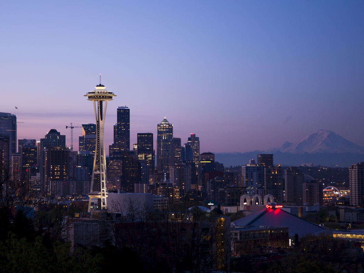 Seattle skyline at dusk featuring the Space Needle, with the cityscape and Mount Rainier in the background against a twilight sky.