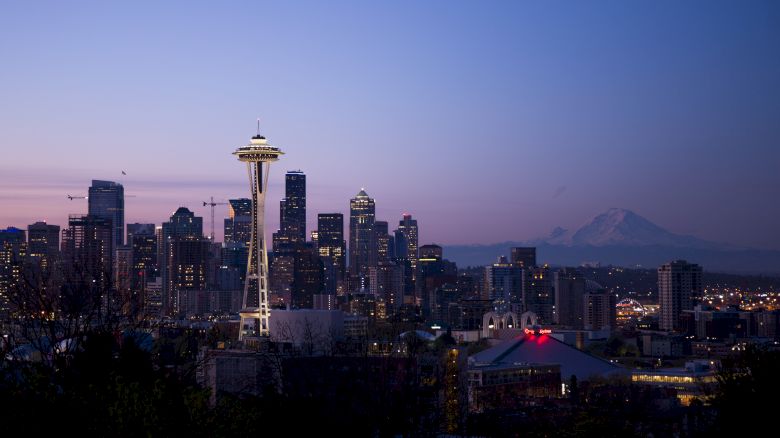 Seattle skyline at dusk featuring the Space Needle, with the cityscape and Mount Rainier in the background against a twilight sky.